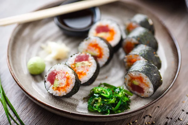 Sushi maki broodjes met tonijn, vliegende vis kaviaar, krab, avocado op een bord met eetstokjes, sojasaus, wasabi en gember. Japans traditioneel eten closeup geserveerd voor de lunch in modern gastronomisch restaurant — Stockfoto