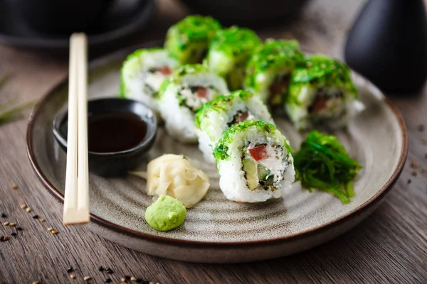 Sushi maki broodjes met komkommer, avocado, tomaat, romige kaas, chuka wakame op een bord met stokjes, sojasaus, wasabi en gember. Japanse traditionele zeevruchten geserveerd voor lunch in restaurant — Stockfoto