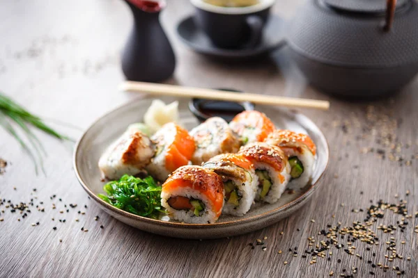 Sushi maki broodjes met zalm, paling, avocado, komkommer op een bord met stokjes, sojasaus, wasabi en gember. Japanse traditionele visgerechten close-up geserveerd voor de lunch in modern gastronomisch restaurant — Stockfoto