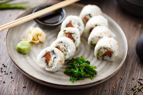 Sushi maki rullar Philadelphia med lax, krämig ost och avokado på en tallrik med ätpinnar, sojasås, wasabi och ingefära. Japanska traditionella skaldjur serveras till lunch i modern restaurang — Stockfoto