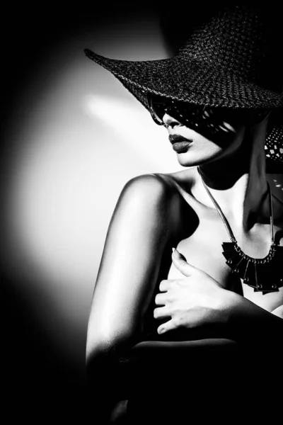 Έννοια μόδας. Πορτρέτο μιας όμορφης γυναίκας με μεγάλο καπέλο και γυαλιά ηλίου σε έντονο φως αντίθεσης. Γυναικείο μοντέλο που φοράει αξεσουάρ ποζάρει στο στούντιο. Επαγγελματικό μακιγιάζ. Μαύρο και άσπρο μονόχρωμο — Φωτογραφία Αρχείου