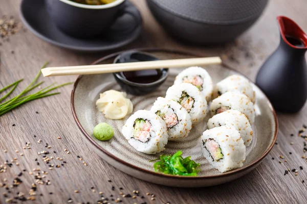 Sushi maki rolls California s krabem, okurkou a avokádem na talíři s hůlkami, sójovou omáčkou, wasabi a zázvorem. Japonské tradiční mořské plody podávané k obědu v moderní gurmánské restauraci — Stock fotografie