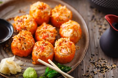 Somon, yengeç, salatalık, avokado, uçan balık yumurtası ve yemek çubuğu, soya sosu, wasabi ve zencefilli baharatlı soslu fırında suşi ruloları. Japon deniz ürünleri restoranda öğle yemeği için servis edilir.