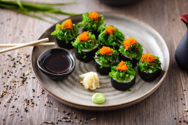 Yengeç, yosun salatası ve yemek çubuğu, soya sosu, wasabi ve zencefilli uçan balık yumurtası ile suşi maki ruloları. Geleneksel Japon deniz ürünleri modern gurme restoranında öğle yemeği olarak servis edilir.