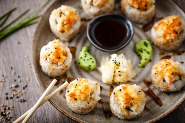 Pişmiş suşi maki ruloları, karides ve yengeç ile birlikte yemek çubuğu, soya sosu, wasabi ve zencefil. Japon geleneksel balık yemekleri modern gurme restoranında öğle yemeği için servis edilir..