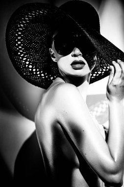 Moda konsepti. Büyük şapkalı ve parlak kontrastlı güneş gözlüklü güzel bir kadının portresi. Stüdyoda aksesuar giyen kadın model. Profesyonel makyaj. Siyah ve beyaz tek renk.