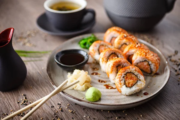 Bakade sushi maki rullar med lax, krabba och kryddig sås på en tallrik med ätpinnar, sojasås, wasabi och ingefära. Japansk traditionell fisk mat närbild serveras till lunch i modern gourmet restaurang — Stockfoto