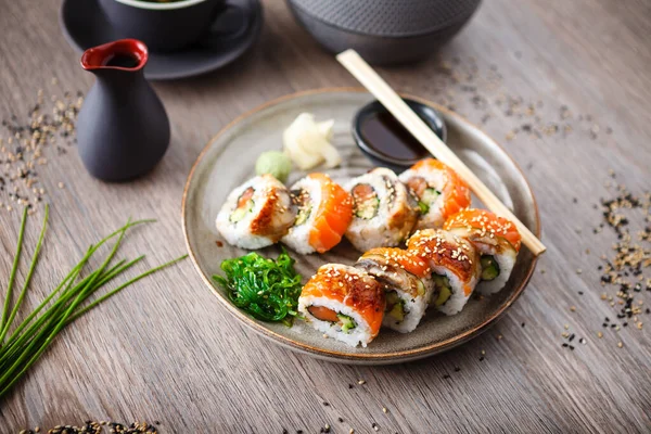 Sushi maki broodjes met zalm, paling, avocado, komkommer op een bord met stokjes, sojasaus, wasabi en gember. Japanse traditionele visgerechten close-up geserveerd voor de lunch in modern gastronomisch restaurant — Stockfoto