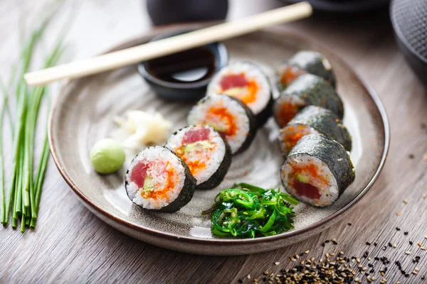 Rouleaux de maki sushi au thon, caviar de poisson volant, crabe, avocat dans une assiette avec baguettes, sauce soja, wasabi et gingembre. Nourriture traditionnelle japonaise servie en gros plan pour le déjeuner dans un restaurant gastronomique moderne — Photo