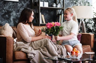 Anne-kız ilişkisi kavramı. Genç bir kız doğum gününde mutlu kadını tebrik eder ve ona çiçekler ve hediye verir. Aile yıldönümünü ya da anneler gününü evde kutlar.