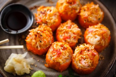 Somon, yengeç, salatalık, avokado, uçan balık yumurtası ve yemek çubuğu, soya sosu, wasabi ve zencefilli baharatlı soslu fırında suşi ruloları. Japon deniz ürünleri restoranda öğle yemeği için servis edilir..