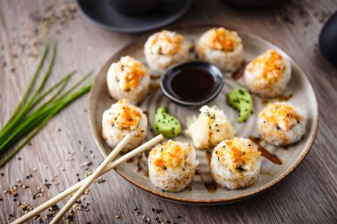 Pişmiş suşi maki ruloları, karides ve yengeç ile birlikte yemek çubuğu, soya sosu, wasabi ve zencefil. Japon geleneksel balık yemekleri modern gurme restoranında öğle yemeği için servis edilir..