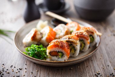 Somon, yılan balığı, avokado soslu suşi çubuklu salatalık, soya sosu, wasabi ve zencefil. Japon geleneksel balık yemekleri modern gurme restoranında öğle yemeği için servis edilir..