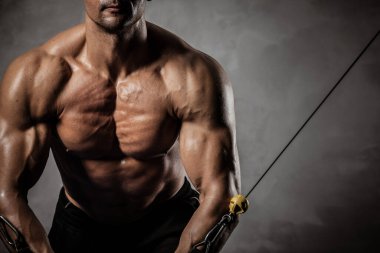 Spor, spor ve sağlıklı yaşam tarzı konsepti. Çıplak gövdeli yakışıklı atletik adam egzersiz yapıyor. Vücut geliştiren erkek model, kaslarını çapraz eğitim aparatında şişiriyor..