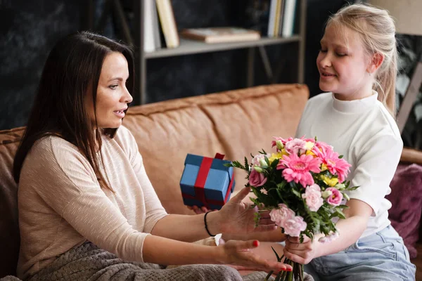Concepto de relación madre e hija. Una adolescente felicita a la mujer feliz en su cumpleaños y le regala flores y regalos. La familia celebra el aniversario o el día de las madres en casa. — Foto de Stock