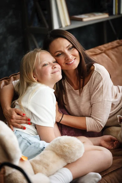 Begreppet mor och dotter. En kvinna och en tonårstjej sitter framför TV:n på soffan och har roligt och pratar. Familjen tillbringar tid hemma. Liten hund som ligger på varv — Stockfoto