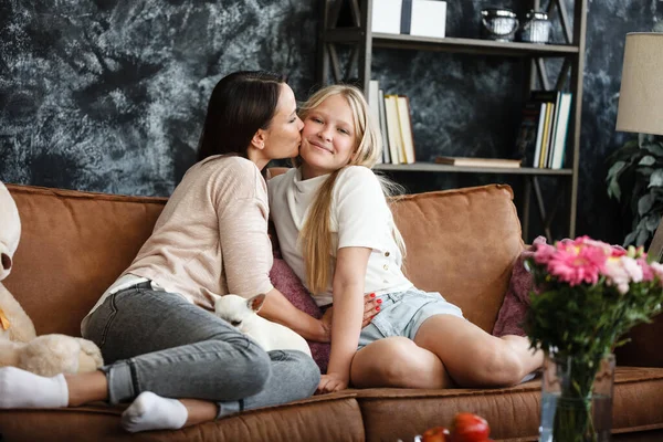 Koncept vztahu mezi matkou a dcerou. Žena a dospívající dívka sedí před televizí na gauči a baví se. Rodina tráví čas doma. Malý pes ležící na klíně — Stock fotografie