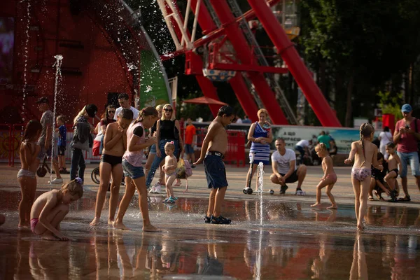Yaz eğlencesi. Mutlu çocuklar koşar, jetlerin arasında oynar ve fıskiyeye su sıçratır. Şehir parkında yaz günü. Kharkiv, Ukrayna. 08.08.2021