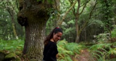 Kadının ve iki köpeğinin eğrelti otlarıyla yemyeşil bir ormanda yürürken çekilmiş bir fotoğrafı. Kadın siyah gömlek ve pantolon giyiyor..