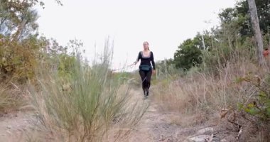 Düşük açılı bir kadın ve iki köpeği bir ormanın yanındaki tarlada yürürken kadın siyah bir gömlek ve siyah pantolon giyiyor..