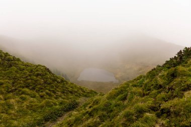 Azores 'in ortasında gölü olan sisli bir dağ vadisi. Göl çimenler ve ağaçlarla çevrilidir. Gökyüzü bulutlu, ortama huzurlu ve huzurlu bir atmosfer veriyor.