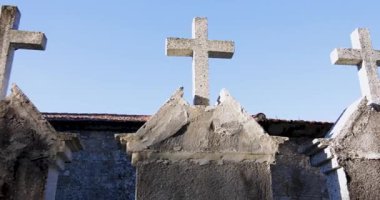 A cemetery with a row of white crosses. The sun is shining on the cemetery, creating a peaceful and somber atmosphere