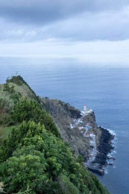 Uzakta deniz feneri olan güzel bir okyanus manzarası. Gökyüzü bulutlu, ama su sakin.