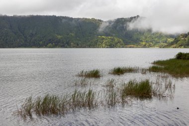 Üzerinde bulutlu bir gökyüzü olan bir göl. Su sakin ve gökyüzü kapalı.