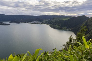 Sete Cidades, Azores 'de arkasında yeşil bir tepe olan güzel bir göl. Göl sakin ve huzurlu. Gökyüzü bulutlu, ama güneş hala bulutların arasında parlıyor..