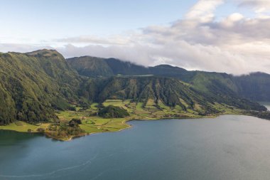 Sete Cidades, Azores 'de önünde bir göl olan güzel bir dağ sırası. Göl yeşil tepeler ve ağaçlarla çevrilidir. Gökyüzü açık ve güneş parlıyor.