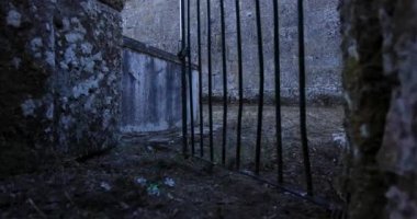 A gate with a stone wall behind a Romanesque church with a bell tower. The gate is made of metal and is open. The stone wall is grey.