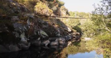 Bir köprü kayalık bir kıyı şeridine sahip bir nehri kapsar. Köprü ahşap ve o yaşlı. Su sakin ve köprünün yansıması suda görülebiliyor. Huzurlu ve huzurlu bir sahne.