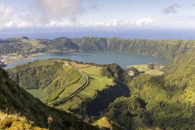 Sete Cidades, Azores 'de güzel bir göl ve dağ manzarası. Göl yeşil tepeler ve ağaçlarla çevrilidir. Gökyüzü açık ve güneş parlıyor. Huzurlu ve huzurlu bir sahne.