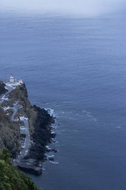 Uzakta deniz feneri olan güzel bir okyanus manzarası. Su sakin ve gökyüzü mavi ve beyaz karışımı.