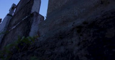 Çan kulesi olan bir kilise kulesi. Gökyüzü açık ve mavi. Kilise eski ve taştan bir dış görünüşü var.