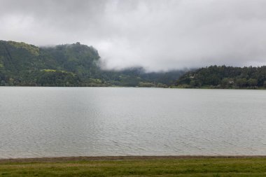 Arkasında bulutlu bir gökyüzü olan bir göl. Su sakin ve gökyüzü kapalı.
