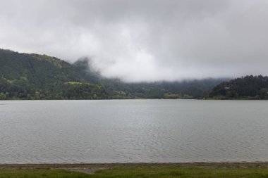 Arkasında bulutlu bir gökyüzü olan bir göl. Su sakin ve gökyüzü kapalı.
