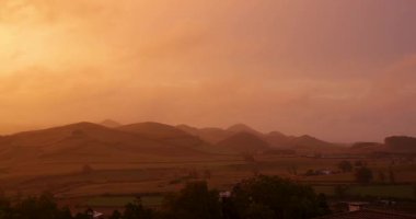 Capelas, Azores 'te evleri ve tepesi olan küçük bir kasabanın üzerinde güzel bir günbatımı. Gökyüzü turuncuya boyandı ve güneş batıyor. Sol atış dönüyor.