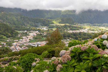 Altında bir kasaba olan yemyeşil bir yamaç. Kasaba küçük ve birkaç evi var. Tepe, çiçek ve bitkilerle kaplı. Bu da Furnas, Azores 'deki manzarayı huzurlu ve sakin bir atmosfere sokuyor.