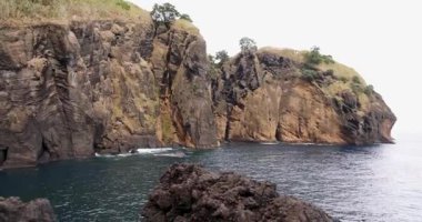 Atlantik Okyanusu kıyısındaki dik volkanik kayalıklar Capelas, Azores 'deki mavi sudan yükseliyor. Su sakin ve gökyüzü bulutlu. Yaya aşısı..