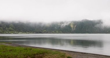 Furnas lagününün arka planında bir gölle sisli bir gün, Azores. Su sakin ve gökyüzü kapalı.