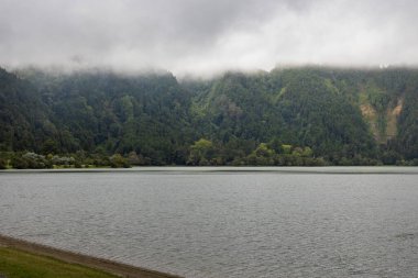 Üzerinde bulutlu bir gökyüzü olan bir göl. Su sakin ve gökyüzü kapalı.