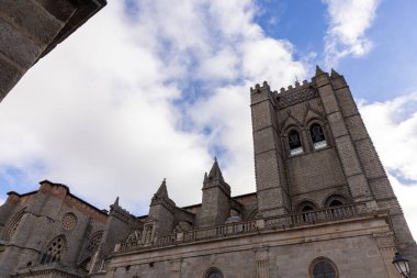 Saat kulesi ve çan kulesi olan büyük taştan bir bina. Binanın etrafı taştan bir duvarla çevrili ve büyük bir kemer yolu var. Gökyüzü bulutlu ve güneş bulutların arasında parlıyor.