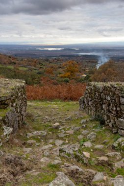 Uzakta ateşi olan bir köy manzarası. Yangın arka planda ve köy ön planda.