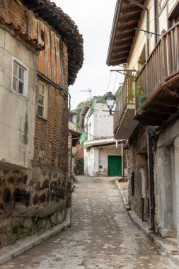 Cuevas del Valle, Avila, İspanya, 10 Aralık 2025: yeşil kapısı ve beyaz binası olan dar bir sokak. Sokak taştan binalarla kaplı ve kaldırım taşı yolu var.