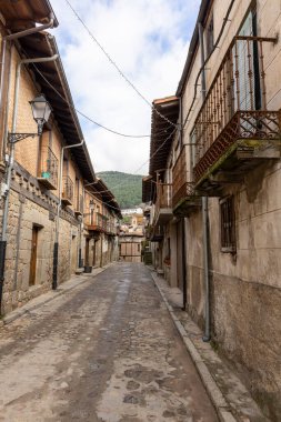 Cuevas del Valle, Avila, İspanya, 10 Aralık 2025, her iki tarafında taş duvar olan dar bir sokak. Sokaklar ıslak ve gökyüzü bulutlu.