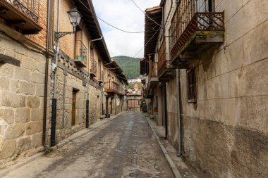Cuevas del Valle, Avila, İspanya, 10 Aralık 2025, yan tarafında tuğla duvar olan dar bir sokak. Sokak ıslak ve kaldırım taşı yüzeyi var.