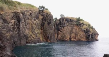 Atlantik Okyanusu kıyısındaki dik volkanik kayalıklar Capelas, Azores 'deki mavi sudan yükseliyor. Su sakin ve gökyüzü bulutlu. Eğil..