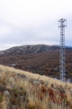 Arka planda dağ olan bir tarlada uzun bir kule duruyor. Gökyüzü bulutlu ve tarla kuru ve kahverengi.