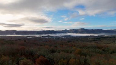 Gökyüzü bulutlu ve güneş batıyor. Ağaçlar yapraklarla kaplı ve dağlar Orense, İspanya 'da arka planda..